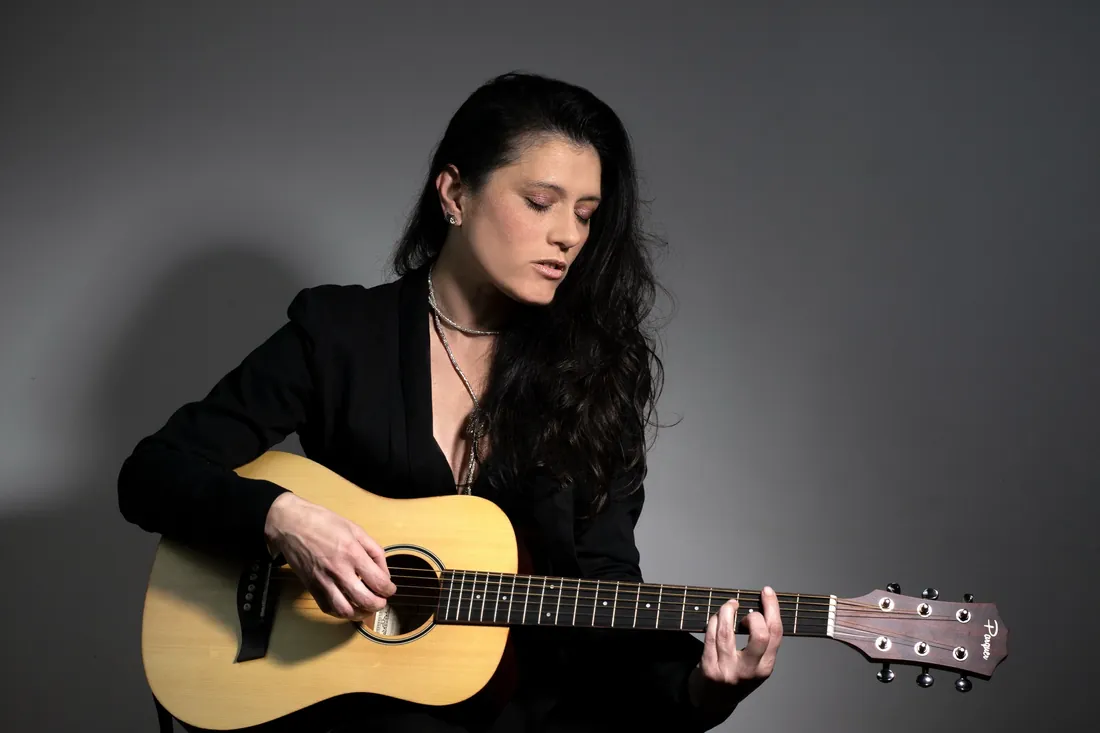 Mujer tocando una guitarra criolla sobre fondo gris