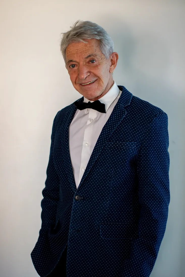 Hombre mayor sonriente con saco azul a lunares y moño